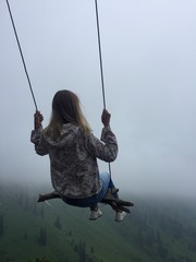 girl with blond hair sitting on a swing in the fog over the precipice, challenge. Kazakhstan, Alma-ATA. Welcome to Kazakhstan!sport lifestyle