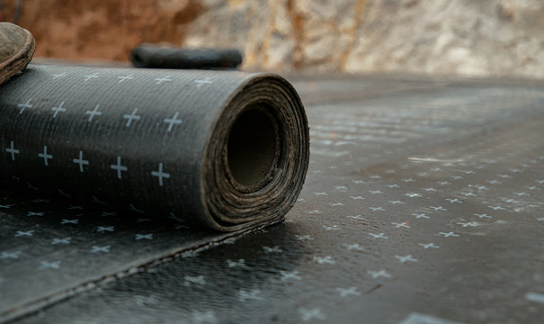 CLOSE UP: Worker rolls out tar paper with his foot while waterproofing a house.