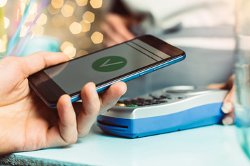 Customer hand pays with smartphone in store using NFC technology. Mobile phone paying the bill with contact less technology.