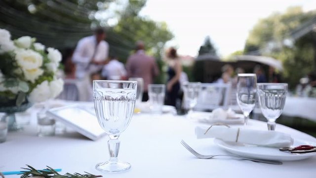 Fashionable wedding table decoration with white flower bouquets of roses and eustoma slow motion closeup, outdoor restaurant background