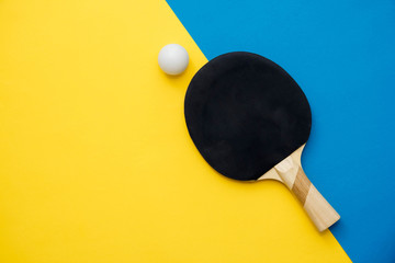 Table tennis or ping pong racket and ball on blue and yellow background. Top view. Copy, empty...