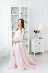 Young pretty woman with white hair waiting for baby, standing in the middle of the room in a beautiful dress. Motherhood
