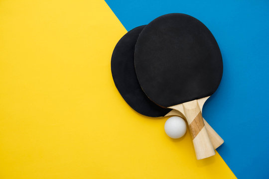 Two table tennis or ping pong rackets and ball on blue and yellow background. Top view. Copy, empty space for text
