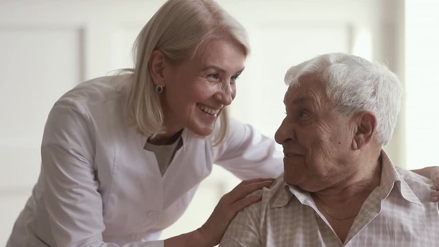 Smiling mature kind woman nurse talking to disabled elder man