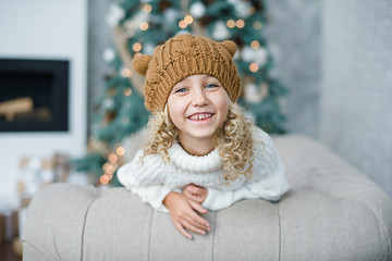 girl in knitted hat near christmas tree makes a wish for new year.