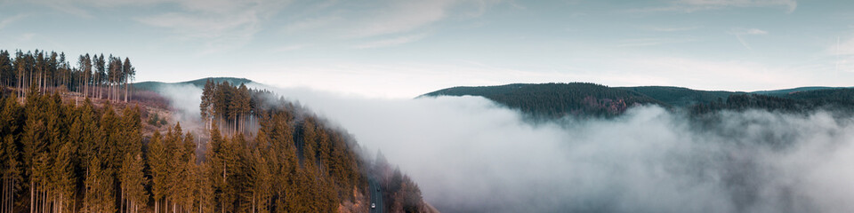 Fototapeta premium Fog and clouds in the valley of a mountain lake. Flying over a mountain nature landscape with view from above. Harz Mountains