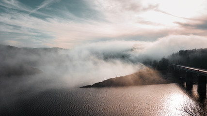 Aerial drone view of heavy fog clouds coming in over the mountain forest with tree silhouettes in the mist. Foggy clouds hanging in the mountains. - Powered by Adobe
