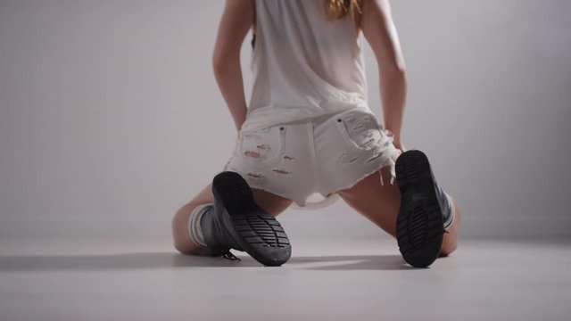 Low section back view shot of female dancer in ripped shorts and grunge boots shaking her buttocks and dancing twerk on her knees in studio filled with fog