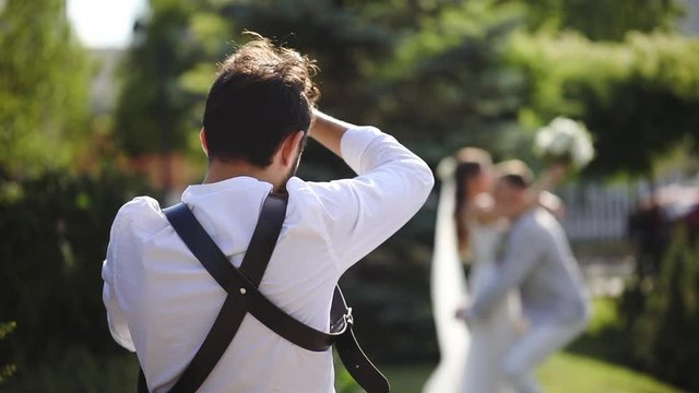 Professional photographer makes photos of wedding couple, green garden background, backside view