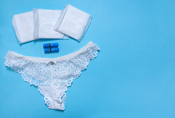 Obraz premium 1 women's white lace panties, sanitary swabs, pads on blue background
