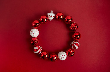 Red Christmas tree toy decoration laid out as a round frame on a red background with copy space. New Year greeting card layout. Minimal style. Flat lay.
