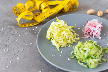 grated vegetables on a plate on a gray background, yellow tape centimeter