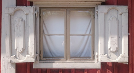 wihite wooden window with shutters in a red woodhouse