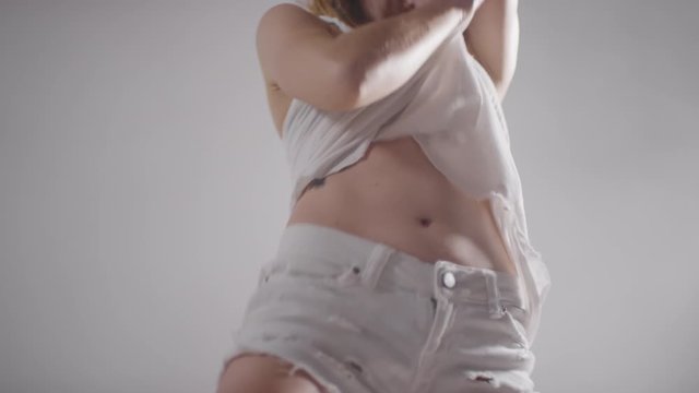 Mid-section shot of seductive tattooed woman in white shorts, bra and sleeveless shirt performing sexy dance in studio filled with fog
