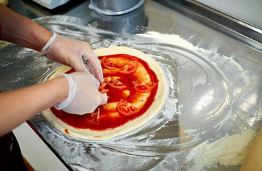 Preparing pizza at restaurant. The chef cooks Italian pizza, topping with sauce.