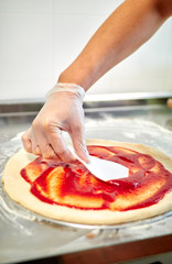 Preparing pizza at home. The chef cooks Italian pizza, topping with sauce.
