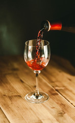 Wine pouring into glass. Wooden and black background 