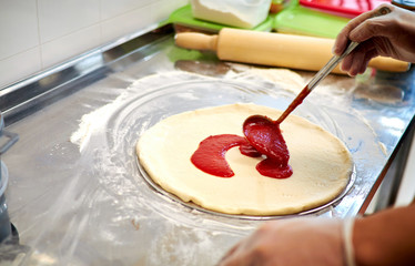 Preparing pizza at home. The chef cooks Italian pizza, topping with sauce.