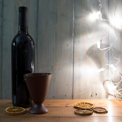 Closed bottle with red wine on a wooden background with decor and a clay glass. Highlighting the background with warm light. Place for text.