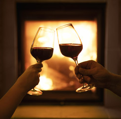 Two glasses of wine on the background of the fireplace, a loving couple with glasses of wine in hand on the background of a burning fireplace, time of love, holiday time.