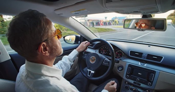Adult bearded guy driving elegant automobile tapping finger over the wheel. Footage for animation. Business class lifestyle. Round sunglasses. Sunny background. Classic casual fashion. Application