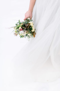 Wedding bouquet with flowers and cotton in hands of the bride. Winter time, snowy forest. Cropped image