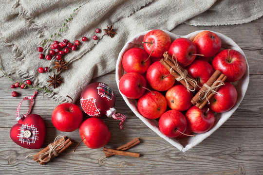 Red apples with cinnamon in a basket in the shape of a heart and cranberries, Christmas balls on a wooden background