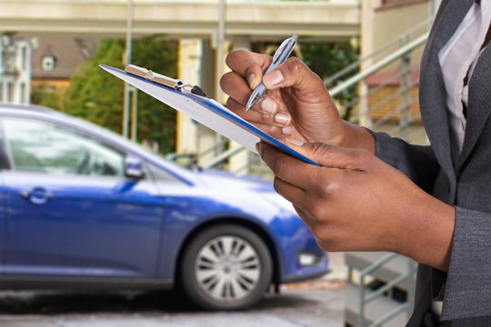Woman's Hands Holding Insurance Paper And Pen Near Blue Car