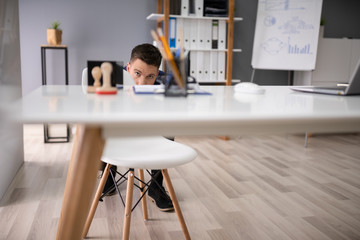 Afraid Businessman Peeking Behind Chair