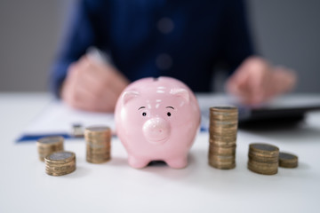 Businessman With Coins And Piggybank Using Calculator