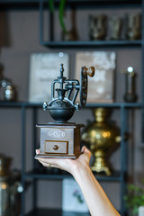 Manual coffee grinder on a small female hand against a background of bolks with samovars and other coffee grinders.