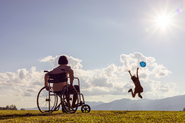 disabled child in a wheelchair and little girl jumping playing with colored balloons at sunset.