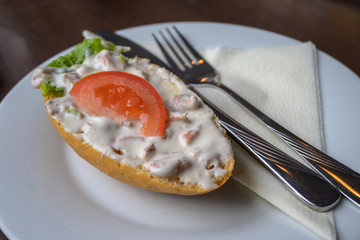 Bread roll or bun with crab salad and tomato served with napkin and cutlery on a white plate