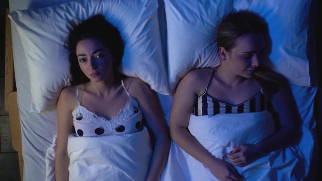 Jealous woman awake at night, calm girlfriend sleeping by, relationship distrust