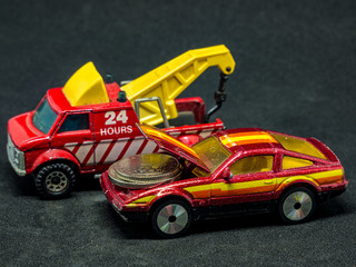 The tow truck with a hook and a car with coins in an open engine cover - small car models (toys)