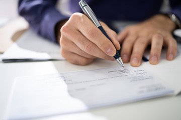 Close Up Of Businessman Filling Blank Cheque At Desk