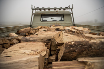 Wood for heating on a car. Back of a truck loaded with chopped wood logs on a grey day.
