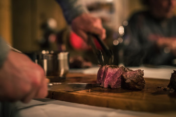 Juicy Medium rare steak being cut with a sharp knife on a wooden board.