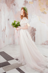 Fototapeta na wymiar Portrait of a young beautiful woman in wedding dress with wreath and bouquet of fresh flowers.