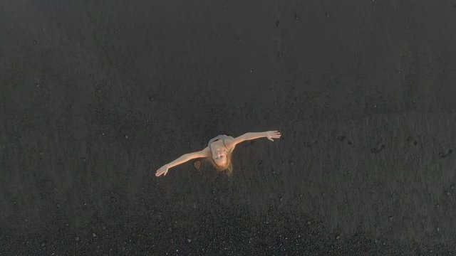 Aerial shot of a young woman walking and having fun on a beach with a black volcanic sand