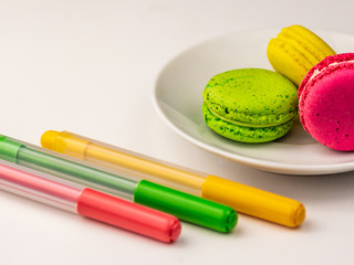 Macaron cakes with matching colorful felt tip pens on a white table
