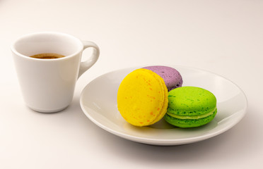 Cup of coffee with colorful macaron cakes in white plate on white table