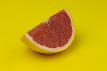 Slice of a red grapefruit isolated on pure yellow background