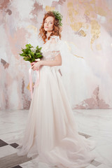 Portrait of a young beautiful woman in wedding dress with wreath and bouquet of fresh flowers.