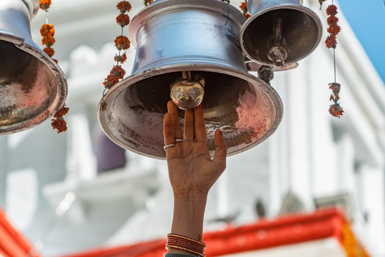 A hand reaching to ring the large temple bells at the temple of Goddess Ganga in Gangotri, India.