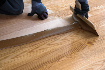 Carpenter master with gloves grouting wooden parquet, phase after sanding