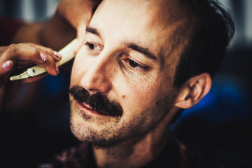 Ein Mann beim Barbier. Sein Vollbart wird gerade mit einem Rasiermesserabgeschnitten. Es bleibt ein...