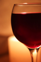 Blurred soft focus bokeh of glass full of red wine glowing from candle light winery background.