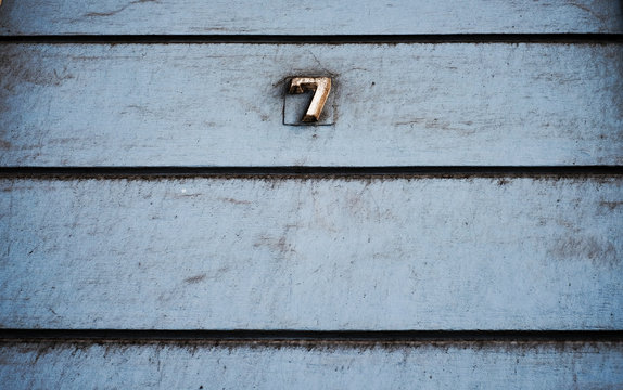 Number 7, seven, on subdued pale blue wall with horizontal black lines, vintage effect.