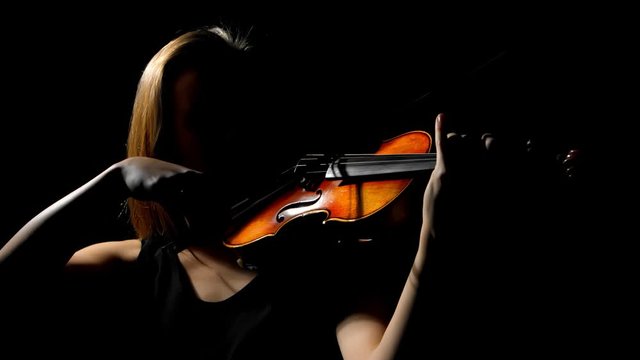 A female performer playing violin isolated on black background. Front view. One light studio set up.Low key studio lighting.